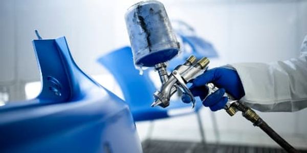 Hand spraying blue paint on a car part with a spray gun.
