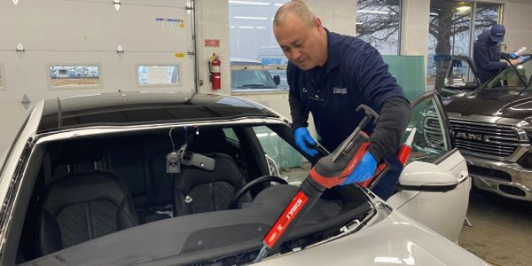 Technician cleaning inside a car using a specialized vacuum tool.