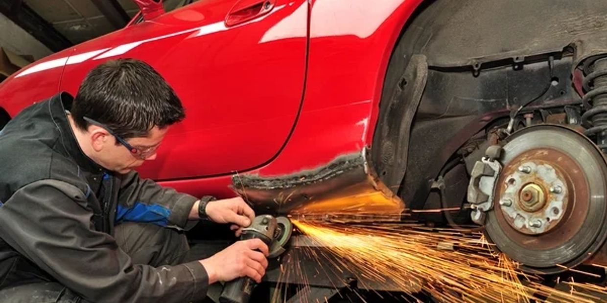 Man grinding car's rusted lower body panel producing sparks.