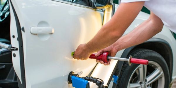 A person using a tool to repair a dent on a white car door.