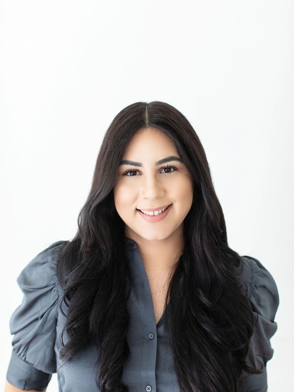 Smiling woman with long dark hair and a gray blouse against a white background.