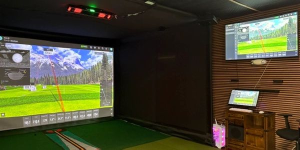 Indoor golf simulator setup with screens displaying golf course and shot data.