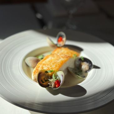 Beautifully plated Halibut filet in broth on a porcelain plate 