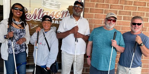 Five people proudly holding their white canes in front of the Mason Jar restaurant