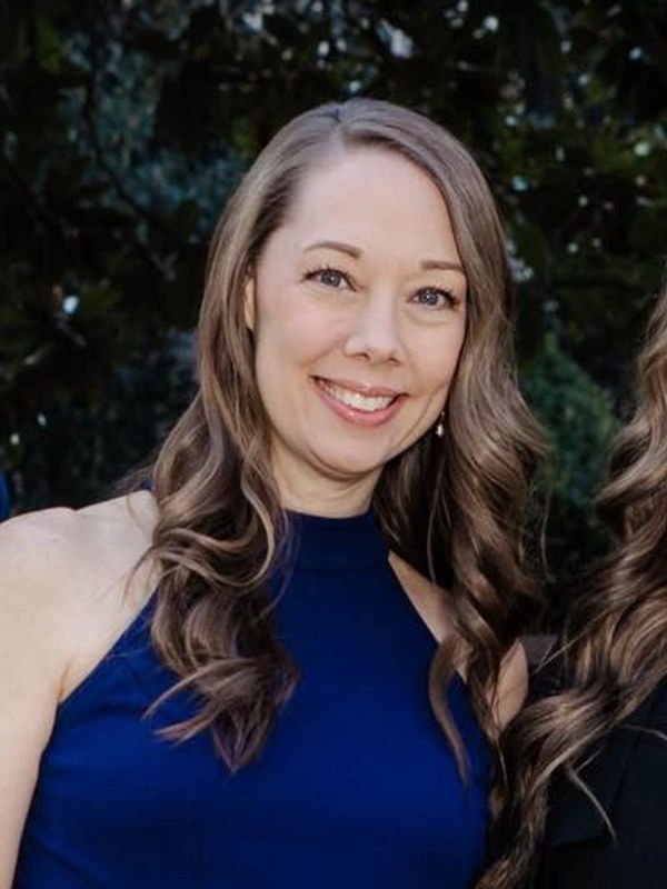 Smiling woman with wavy hair in a blue sleeveless top.