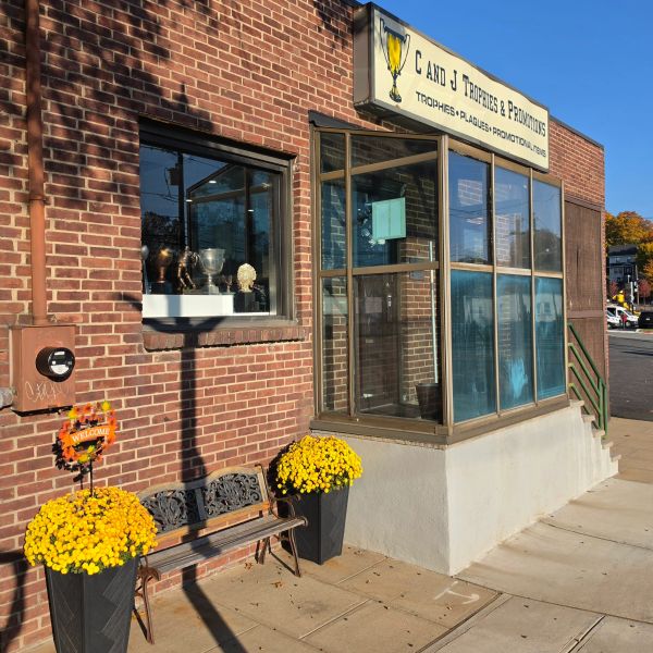 Exterior of a trophy and promotions shop with yellow flowers and bench.