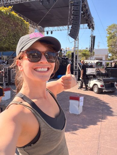 Smiling woman giving thumbs up at an outdoor event setup.