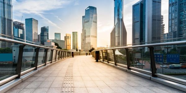 Empty modern pedestrian bridge leading to skyscrapers at sunrise.
