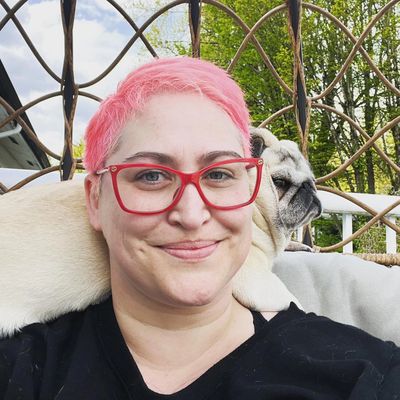 Person with pink hair and glasses smiling with a pug on their shoulder.