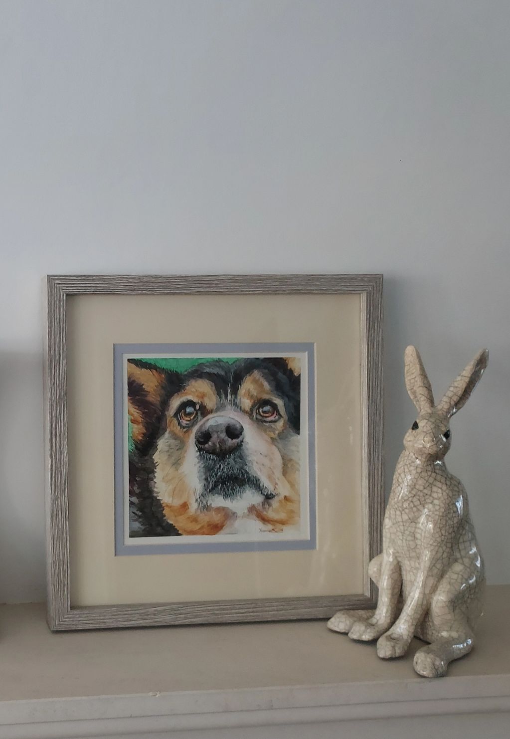 Framed square portrait of close up dog face. Framed on a shelf next to a hare sculpture.