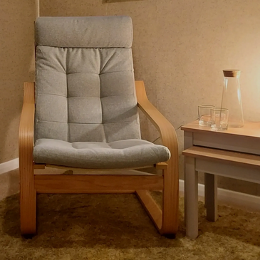 Comfortable soft green hypnotherapy chair in softly lit therapy room. 