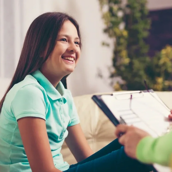 Young girl smiling. She's sitting opposite a female therapist as though they're talking.