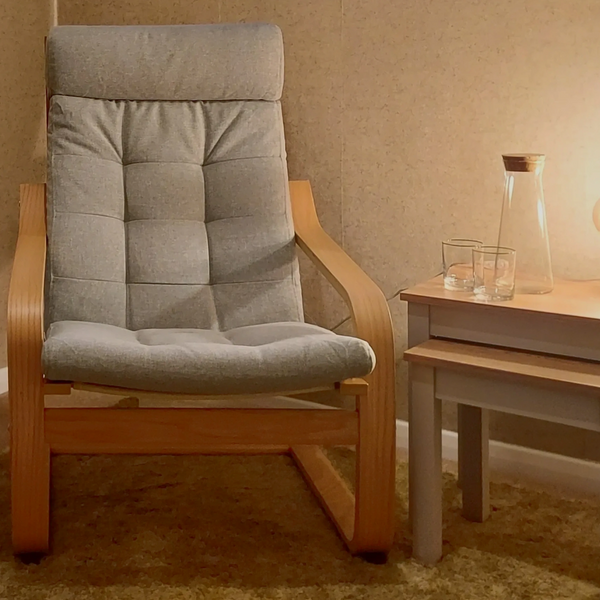 Comfortable hypnotherapy chair in soft lit therapy room with side table and water glasses.