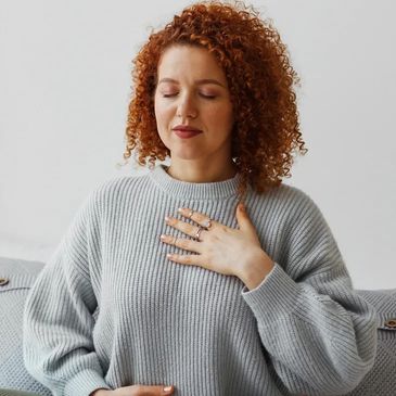 Woman with eyes closed, one hand on chest and one on stomach. Looking calm and relaxed.