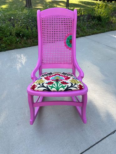 Bright pink rocking chair with floral patterned cushion outdoors.