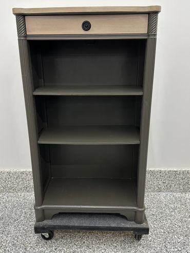 A small wooden shelving unit with three shelves and a drawer on wheels.