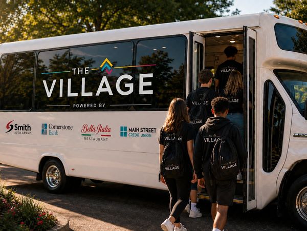 A group of young people boarding a bus labeled The Village.