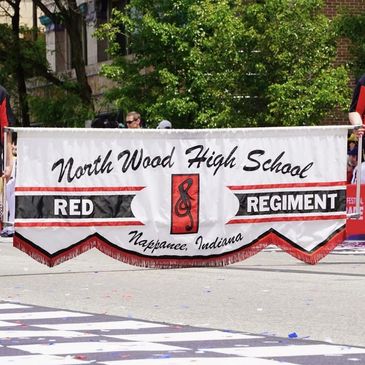 Two people holding a North Wood High School Red Regiment banner in a parade.