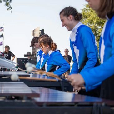 Students in blue uniforms playing percussion instruments outdoors.