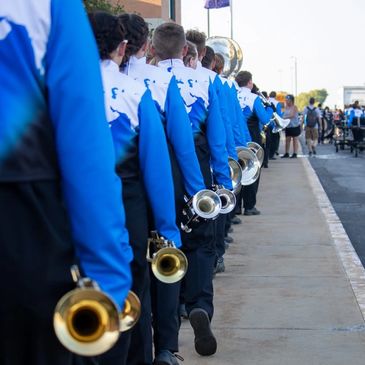 Marching band members in blue uniforms holding brass instruments in a line.
