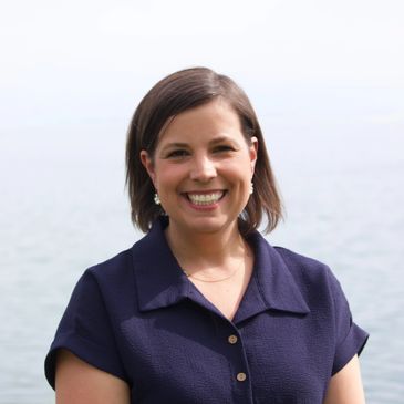 Smiling woman with short brown hair in a navy blue top by the water.