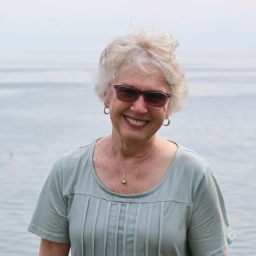 Smiling elderly woman wearing sunglasses by the water.