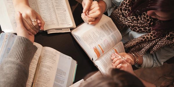 People holding hands in prayer over open Bibles.