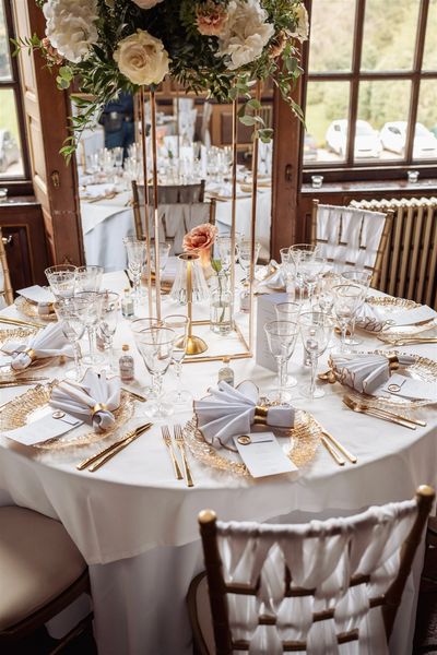Elegant round table set for a formal event with gold accents and floral centerpiece.