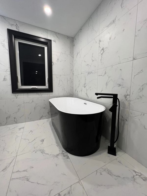 Modern bathroom with a black freestanding bathtub and marble tiles.