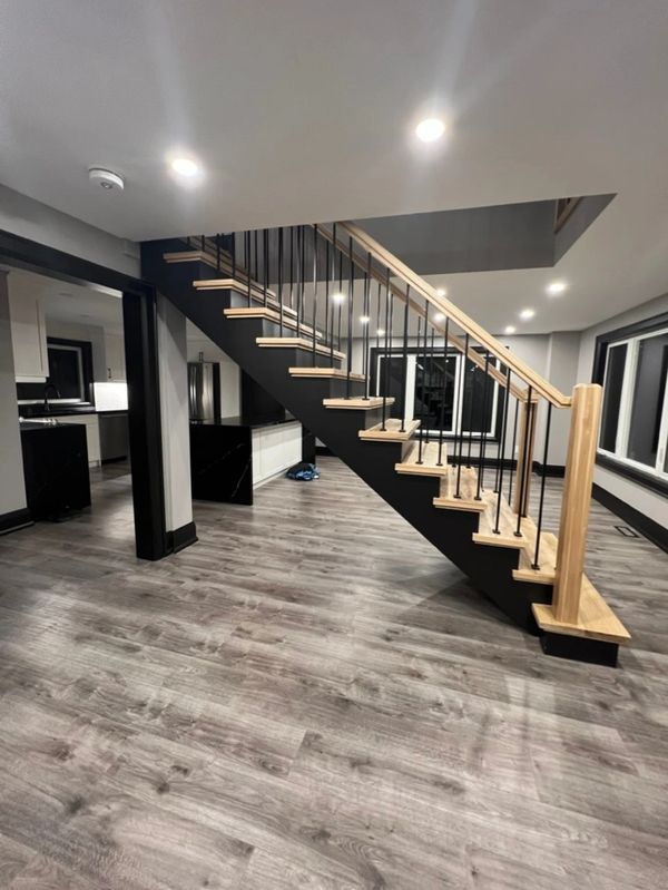 Modern staircase with wood steps and black railing in a spacious room with wood flooring.