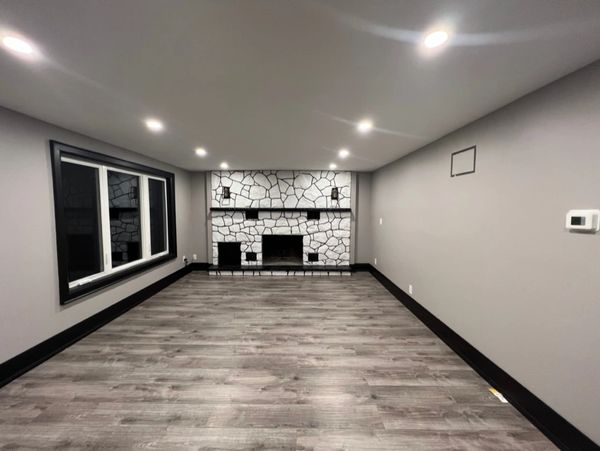 Empty modern room with gray walls, wooden floor, and stone fireplace.