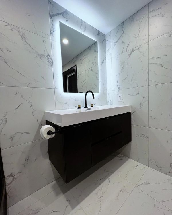 Modern bathroom with marble tiles, floating vanity, and illuminated mirror.
