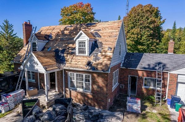 House undergoing roof replacement with old shingles removed and ladders placed.