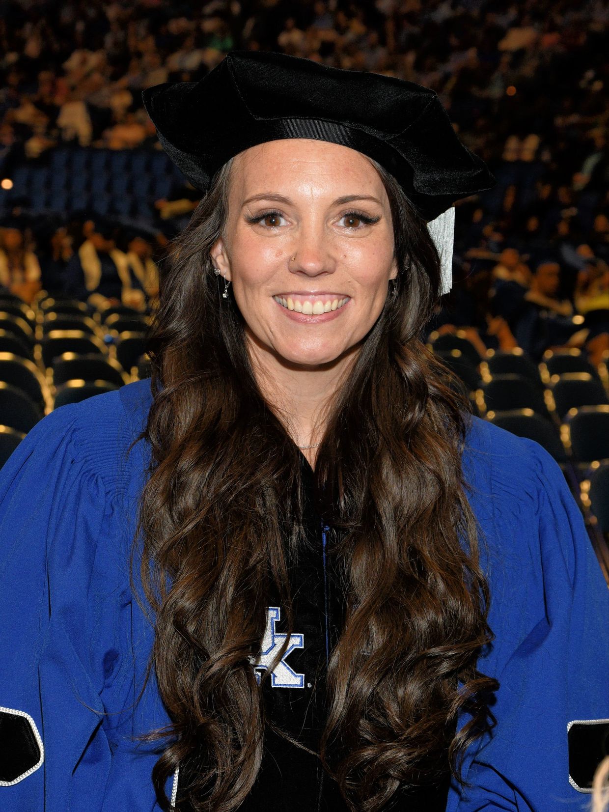 Smiling woman in blue graduation gown and black cap at ceremony.