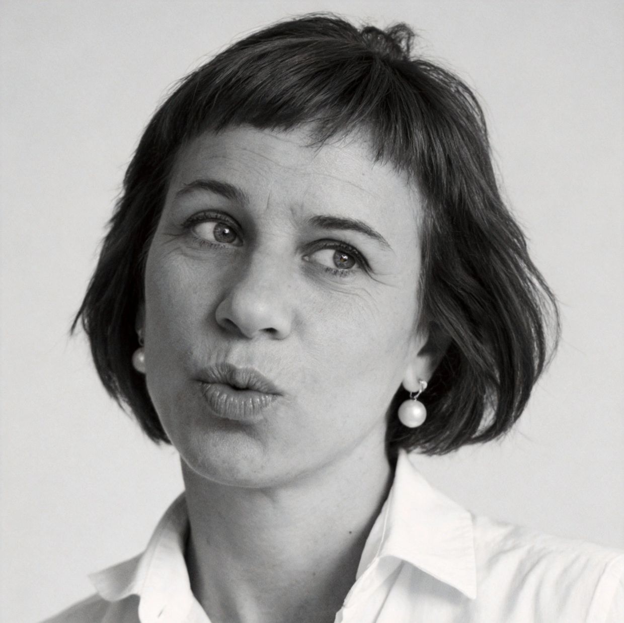 Black and white close-up portrait of a woman with short hair and pearl earrings making a playful expression.