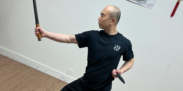 Man practicing martial arts with a sword and dagger indoors.