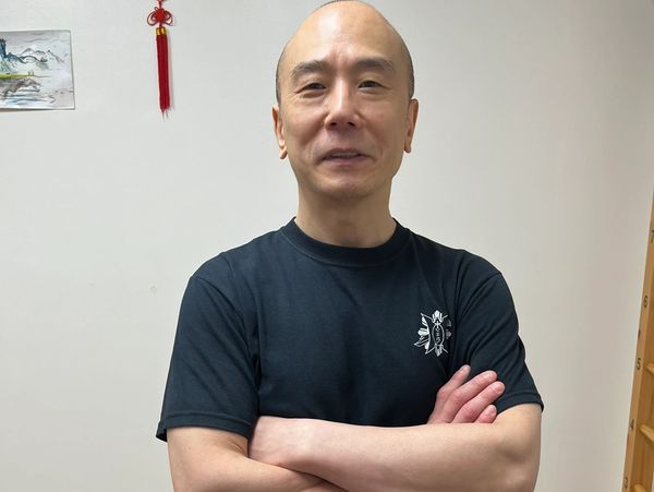 Smiling bald man in a black t-shirt with arms crossed indoors.