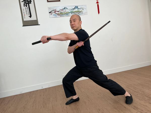 Man practicing martial arts with a baston y daga indoors.