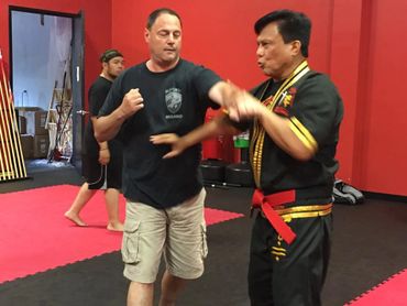 Two men practicing martial arts in a training room with red walls.