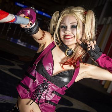Cosplayer dressed as Harley Quinn with a playful smile and bat.