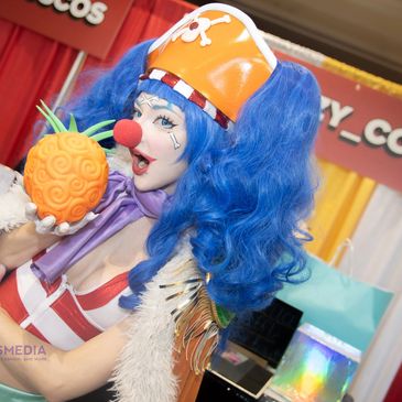 Cosplayer with blue curly hair and pirate hat holding a pineapple prop.