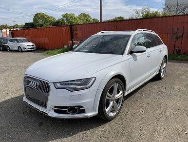 White Audi station wagon parked outdoors near a rusted metal fence.
