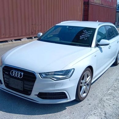White Audi sedan parked beside shipping containers on a sunny day.