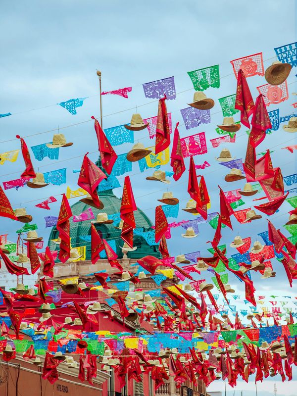 Colorful fabric, hats, and paper flags hanging over a street festival.