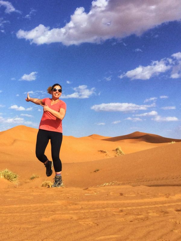 Woman jumping joyfully in the desert under a blue sky.