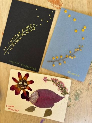 Three cards with pressed flower art on a wooden table.