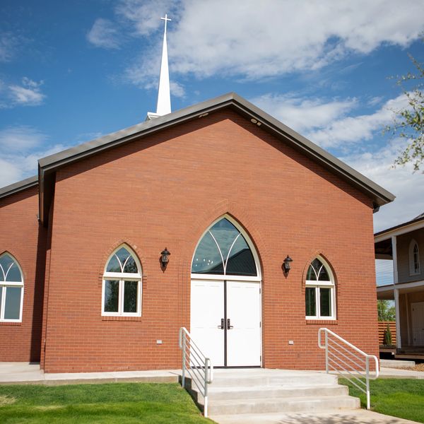 Front view of a red brick church with a white cross on top.
