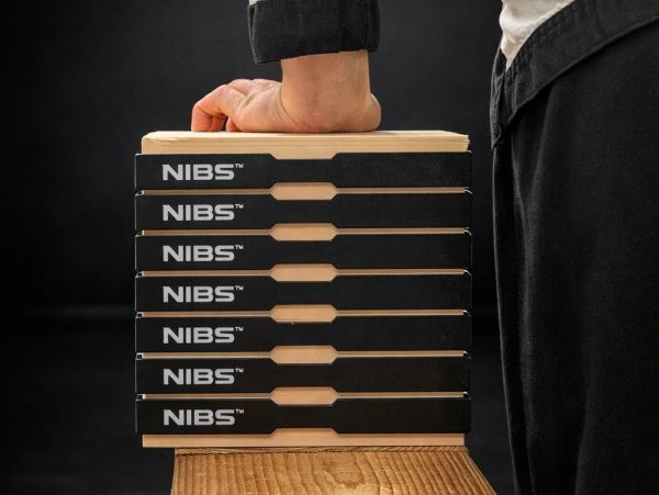 A person presses their fist on a stack of NIBS boxes on a wooden surface.
