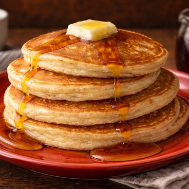 Stack of fluffy buttermilk pancakes topped with melting butter and warm maple syrup