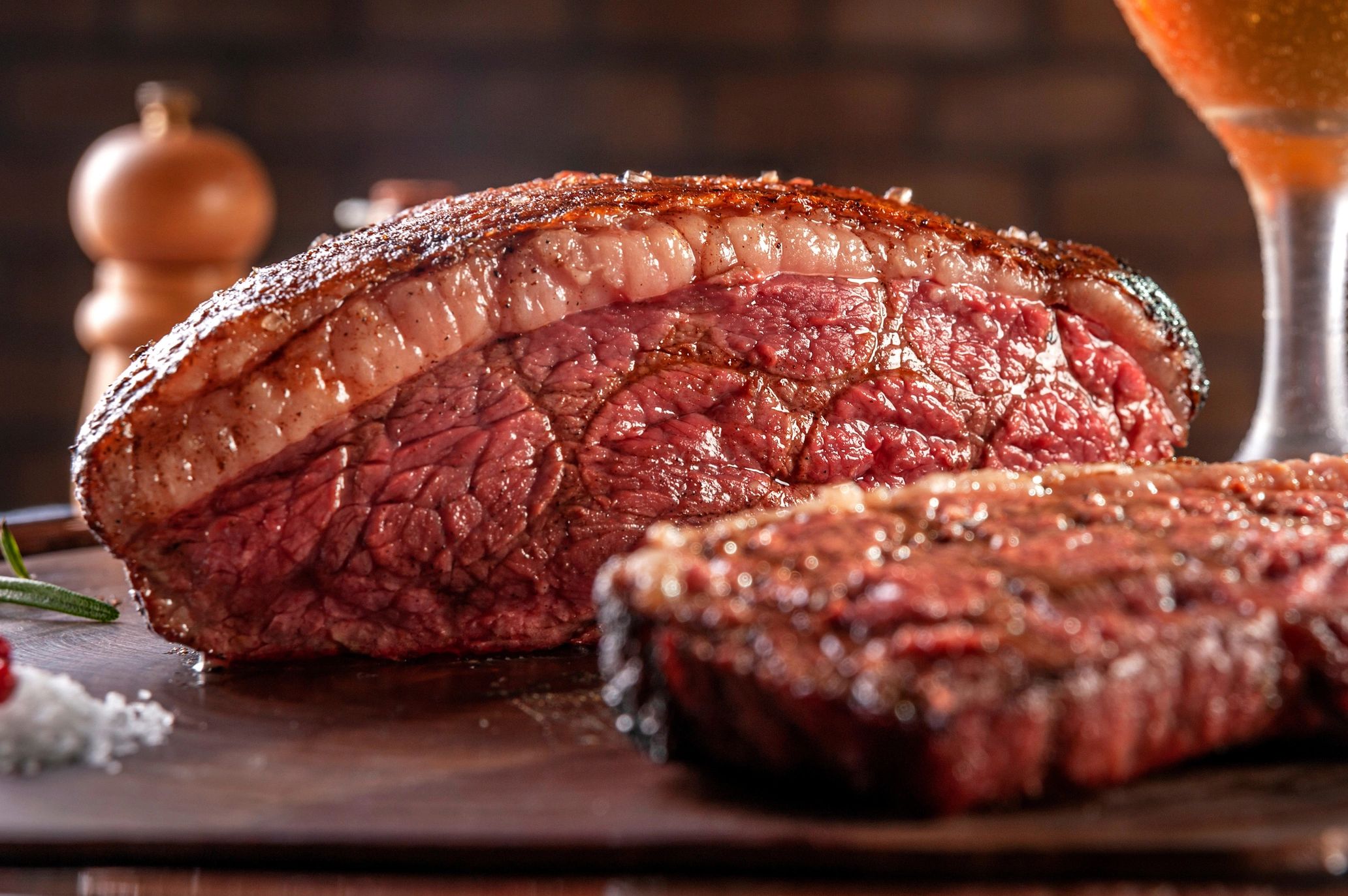 Sliced grilled picanha with a crisp, golden-brown fat cap resting on a wooden cutting board atop a k